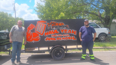 The owner of the company Cody Coppe and a team memeber standing on either side of a trailer with the Haul Yeah Logo and number painted on it