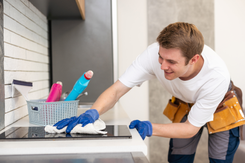 A uniformed man wiping down a countertop with a basket of cleaning supplies next to him, representing professional cleaning services in Hiawatha, KS and Surrounding Areas