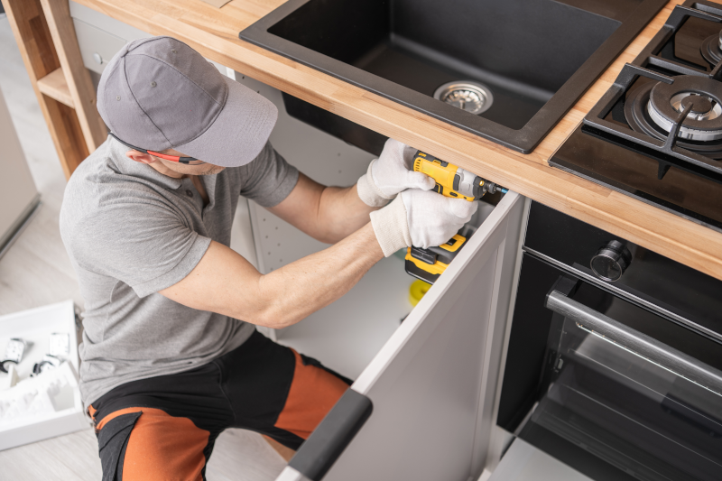 A man using a drill on the door of a lower kitchen cabinet