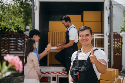 A mover giving a thumbs up while a client signs paperwork with another mover in the background in front of a full move truck in Hiawatha, KS and Surrounding Areas